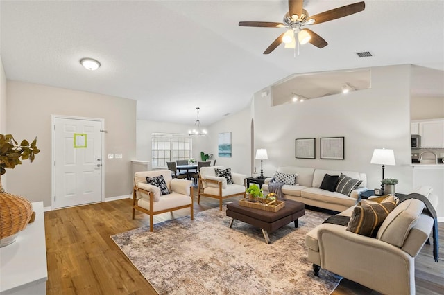 living room with ceiling fan with notable chandelier, lofted ceiling, and hardwood / wood-style floors