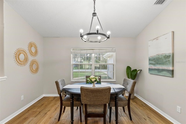 dining area featuring vaulted ceiling, light hardwood / wood-style flooring, and a chandelier