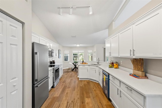 kitchen with sink, kitchen peninsula, white cabinetry, stainless steel appliances, and vaulted ceiling