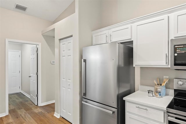 kitchen featuring vaulted ceiling, light hardwood / wood-style flooring, stainless steel appliances, and white cabinets