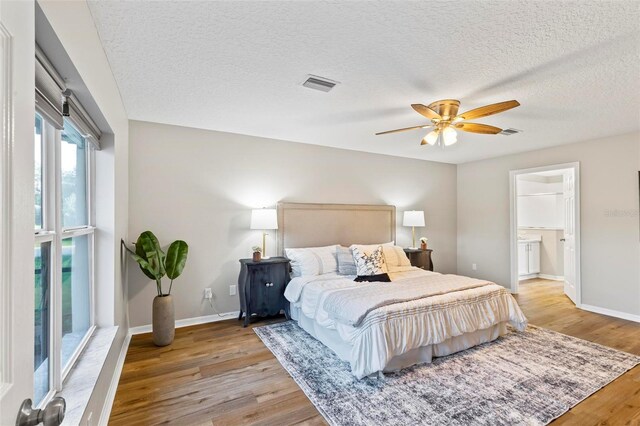 bedroom with ceiling fan, a textured ceiling, light wood-type flooring, and connected bathroom