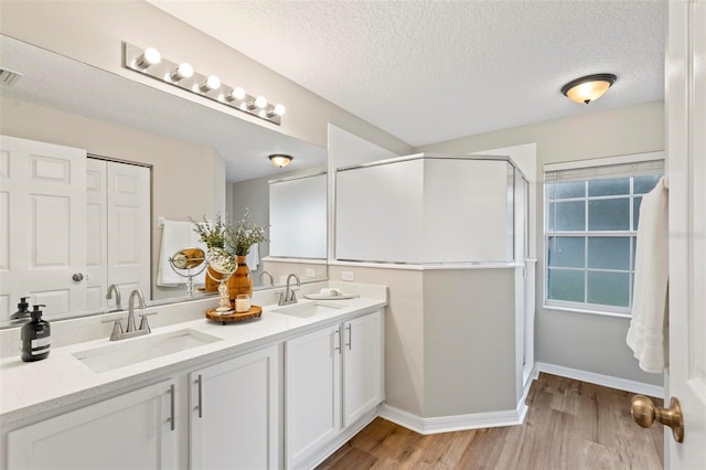 bathroom featuring hardwood / wood-style flooring, a shower with door, vanity, and a textured ceiling