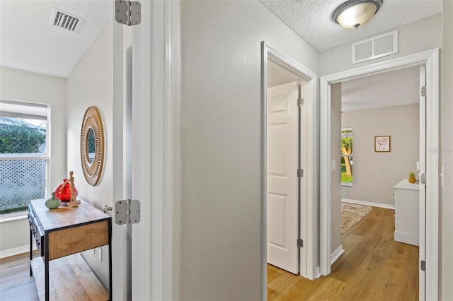 hallway with a textured ceiling and light hardwood / wood-style floors