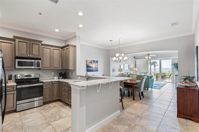 kitchen featuring kitchen peninsula, backsplash, appliances with stainless steel finishes, ceiling fan with notable chandelier, and a kitchen bar