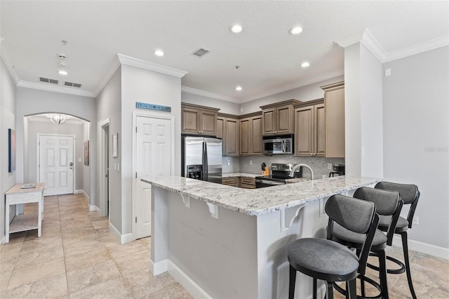 kitchen featuring a breakfast bar, light stone counters, kitchen peninsula, appliances with stainless steel finishes, and crown molding