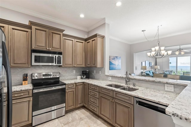 kitchen with light stone counters, ornamental molding, sink, stainless steel appliances, and ceiling fan with notable chandelier