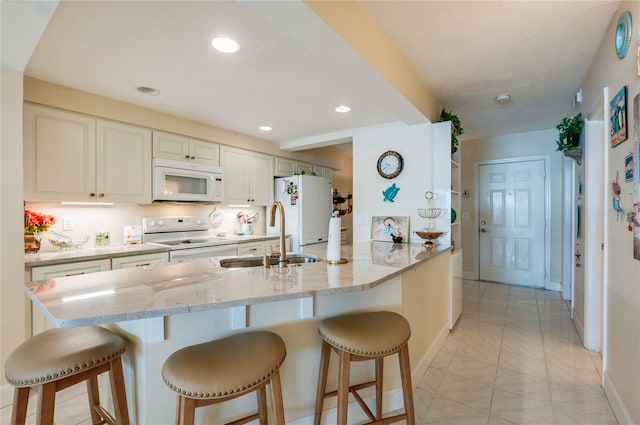 kitchen with white appliances, sink, light stone counters, and a breakfast bar