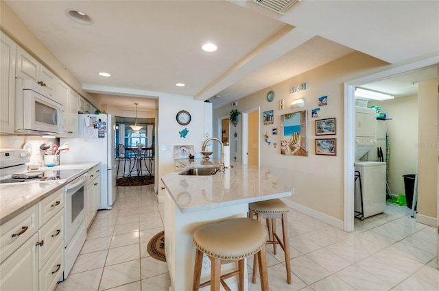 kitchen featuring a kitchen island with sink, a breakfast bar area, sink, white cabinetry, and white appliances