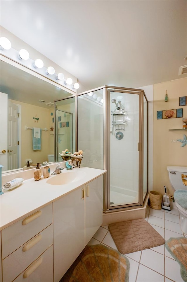 bathroom featuring a shower with door, toilet, vanity, and tile patterned floors