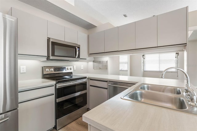 kitchen with appliances with stainless steel finishes, sink, a textured ceiling, gray cabinets, and light hardwood / wood-style flooring