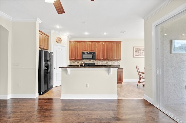 kitchen featuring a kitchen breakfast bar, black appliances, ceiling fan, light hardwood / wood-style flooring, and a kitchen island with sink