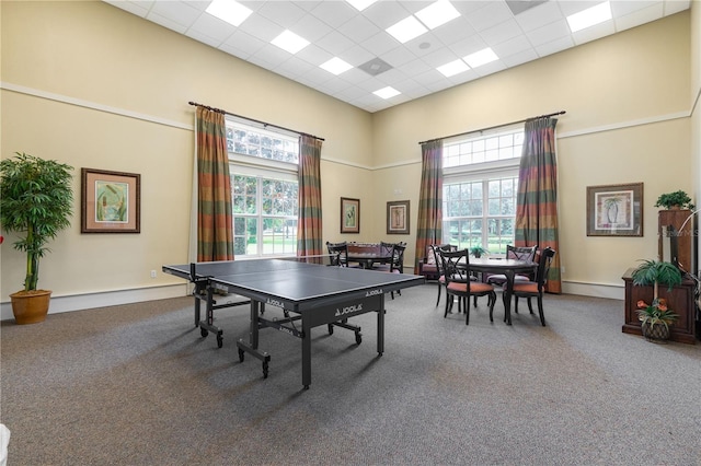 rec room featuring a high ceiling, a healthy amount of sunlight, carpet, and a paneled ceiling