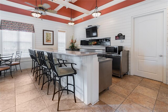 kitchen with kitchen peninsula, hanging light fixtures, a kitchen breakfast bar, wooden walls, and ceiling fan