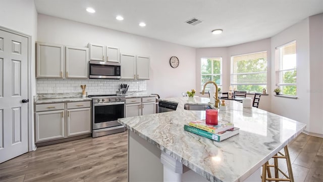 kitchen featuring a kitchen island with sink, appliances with stainless steel finishes, light hardwood / wood-style flooring, and a healthy amount of sunlight