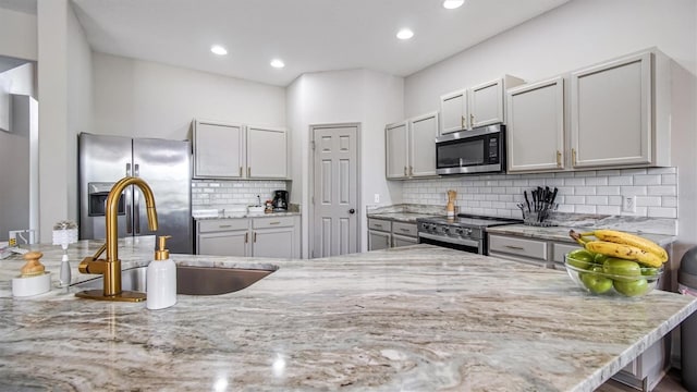 kitchen featuring light stone countertops, stainless steel appliances, decorative backsplash, and sink