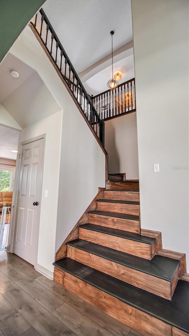 stairway featuring a notable chandelier, vaulted ceiling, and hardwood / wood-style flooring