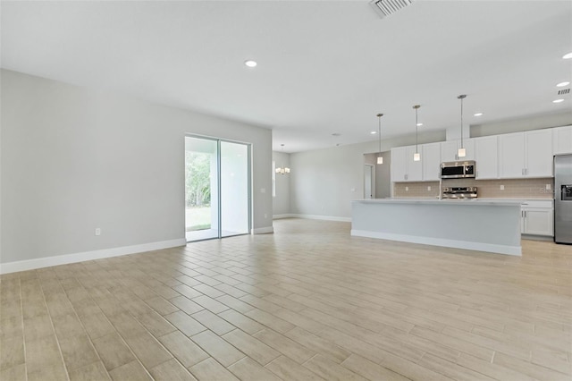 kitchen with appliances with stainless steel finishes, hanging light fixtures, light wood-type flooring, and white cabinetry