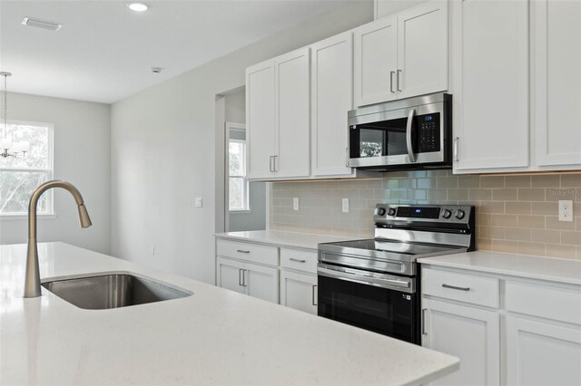 kitchen with appliances with stainless steel finishes, white cabinetry, sink, and pendant lighting