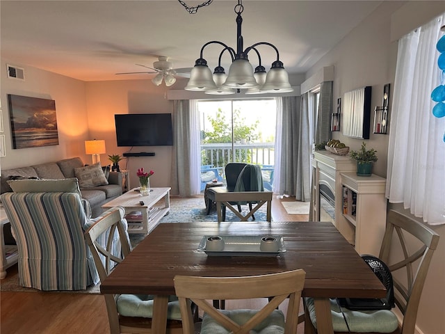 dining space with ceiling fan with notable chandelier and hardwood / wood-style flooring