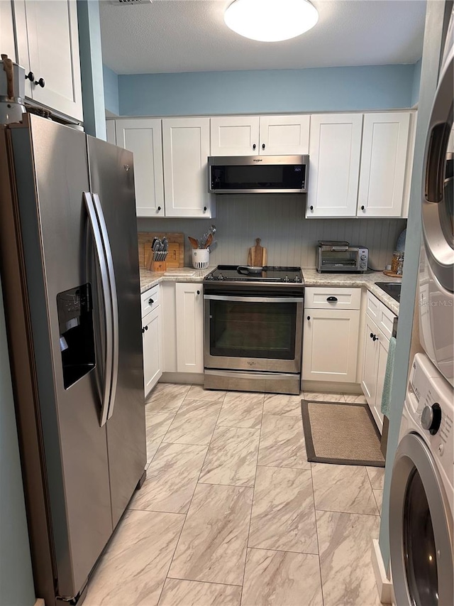 kitchen with stacked washer and dryer, light stone counters, range hood, white cabinets, and appliances with stainless steel finishes