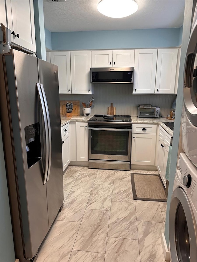610 Ocean Marina Dr Unit 106, Flagler Beach, FL 32136 - kitchen featuring stacked washer and dryer, marble finish floor, white cabinetry, and appliances with stainless steel finishes