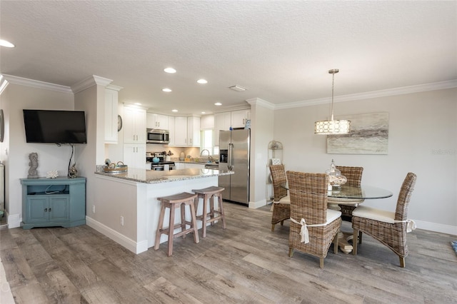 dining area featuring a textured ceiling, light hardwood / wood-style floors, ornamental molding, and sink