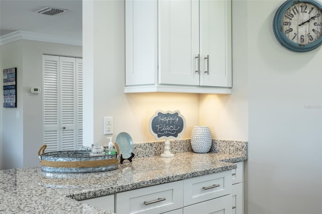 kitchen with light stone counters, ornamental molding, and white cabinetry