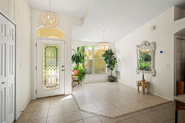 tiled foyer entrance featuring a textured ceiling and a chandelier