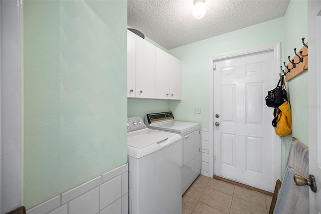 laundry room featuring light tile patterned floors, washing machine and dryer, a textured ceiling, and cabinets