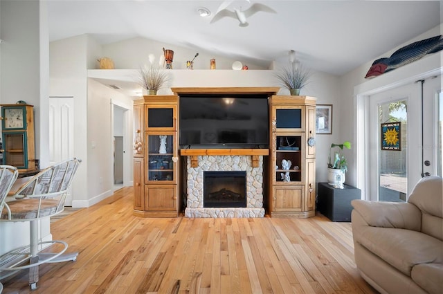 living room with light hardwood / wood-style floors, a stone fireplace, and lofted ceiling