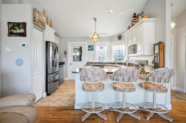 kitchen featuring light hardwood / wood-style floors, a breakfast bar, white cabinets, stainless steel appliances, and decorative light fixtures