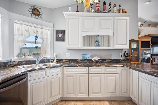 kitchen with white cabinets, lofted ceiling, dark stone counters, stainless steel dishwasher, and sink