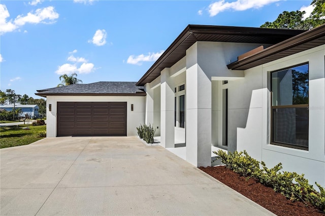 view of side of property with a garage, concrete driveway, a shingled roof, and stucco siding