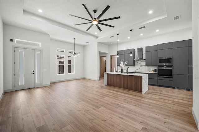 kitchen with a tray ceiling, stainless steel microwave, wall chimney range hood, modern cabinets, and oven