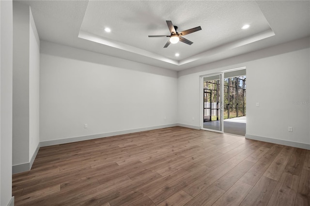 unfurnished room with a textured ceiling, a tray ceiling, wood finished floors, and baseboards