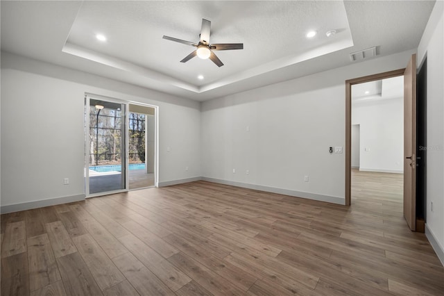 empty room with a tray ceiling, wood finished floors, visible vents, and baseboards