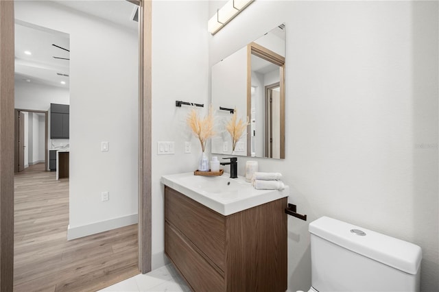 half bath with baseboards, toilet, wood finished floors, vanity, and recessed lighting