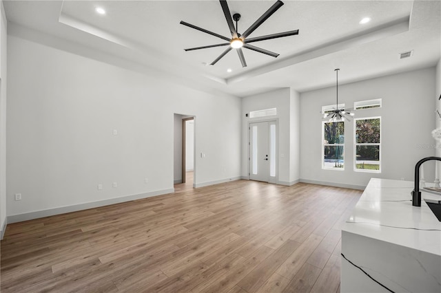 unfurnished living room with recessed lighting, a raised ceiling, light wood-style flooring, and baseboards