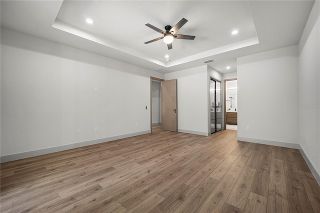 empty room with baseboards, a ceiling fan, a tray ceiling, light wood-style floors, and recessed lighting