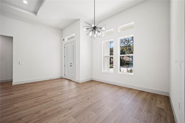 unfurnished dining area with a chandelier, light wood-style flooring, and baseboards