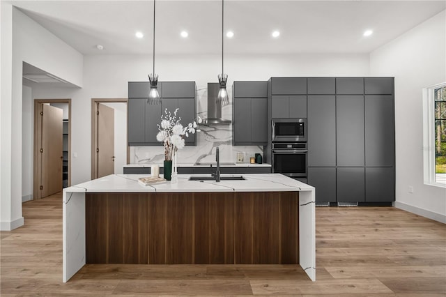 kitchen with stainless steel appliances, gray cabinets, a sink, and wall chimney exhaust hood