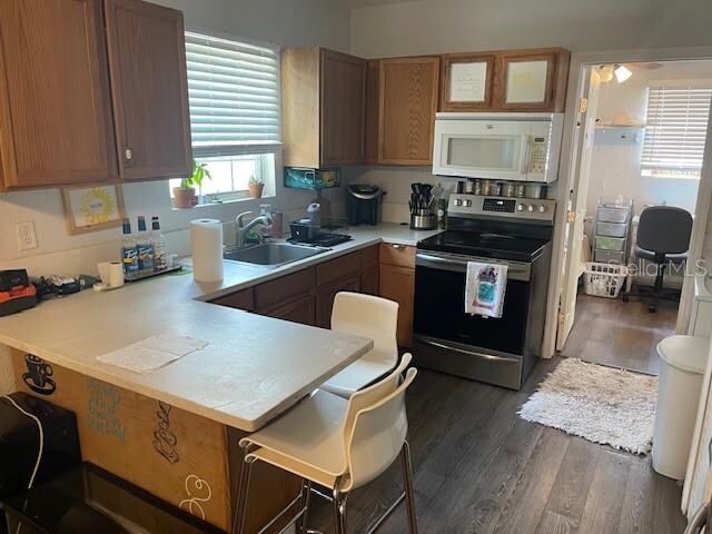 kitchen featuring a breakfast bar, electric range, dark wood-type flooring, sink, and kitchen peninsula