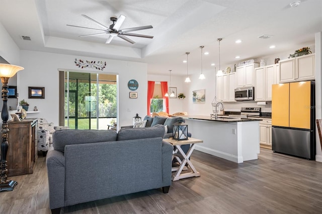 living room with a tray ceiling, dark hardwood / wood-style floors, ceiling fan, and sink