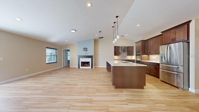 kitchen featuring appliances with stainless steel finishes, hanging light fixtures, vaulted ceiling, backsplash, and a center island with sink