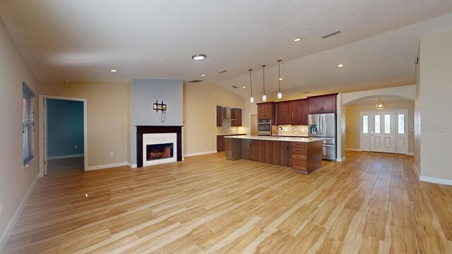 kitchen with vaulted ceiling, decorative light fixtures, stainless steel appliances, a center island, and light hardwood / wood-style floors