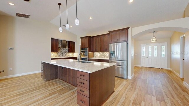 kitchen with pendant lighting, light wood-type flooring, stainless steel fridge with ice dispenser, an island with sink, and vaulted ceiling