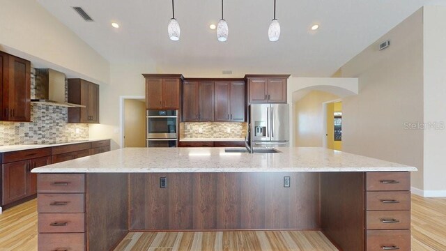 kitchen featuring light wood-type flooring, a center island with sink, stainless steel appliances, and wall chimney exhaust hood