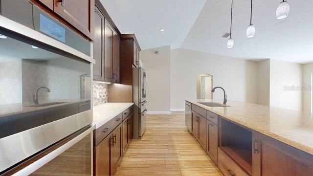 kitchen featuring sink, lofted ceiling, hanging light fixtures, backsplash, and light stone countertops