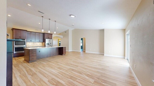 kitchen with stainless steel appliances, light wood-type flooring, lofted ceiling, dark brown cabinetry, and a center island with sink