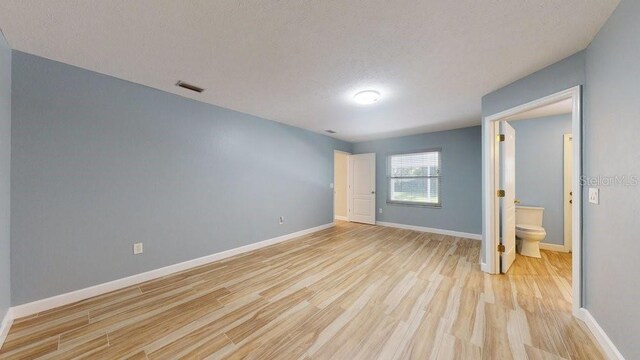 unfurnished bedroom with light wood-type flooring, a textured ceiling, and ensuite bathroom